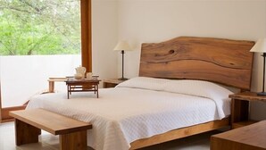 Ein Schlafzimmer mit einem hölzernen Bett, einem Nachttisch, einer Bank und Blick auf Bäume durch ein Fenster.