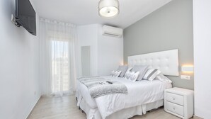 Une chambre à coucher comprenant un lit, des tables de chevet, un téléviseur fixé au mur et un appareil de climatisation.