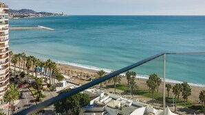 Une vue côtière avec une plage, des palmiers et un bâtiment doté de balcons donnant sur la mer.