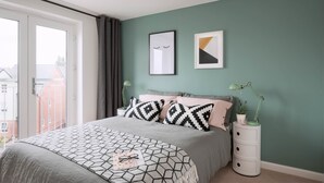Un dormitorio con cama, mesita de noche, lámpara y dos cuadros en la pared.