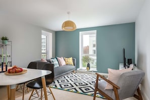 A modern living room with a grey sofa, a dining table with apples, a patterned rug, and a large window. - Canalside Scandinavian - Parking & Netflix (Coventry)