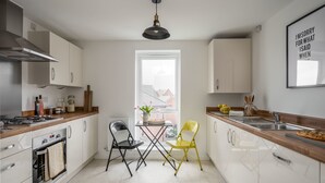 Una cocina moderna con armarios blancos, encimera de madera, una silla negra y amarilla, y un ventanal con vistas a edificios.