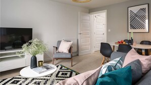 Una sala de estar moderna con televisor, una mesa de centro, una silla, un sofá y un comedor con sillas y una mesa.