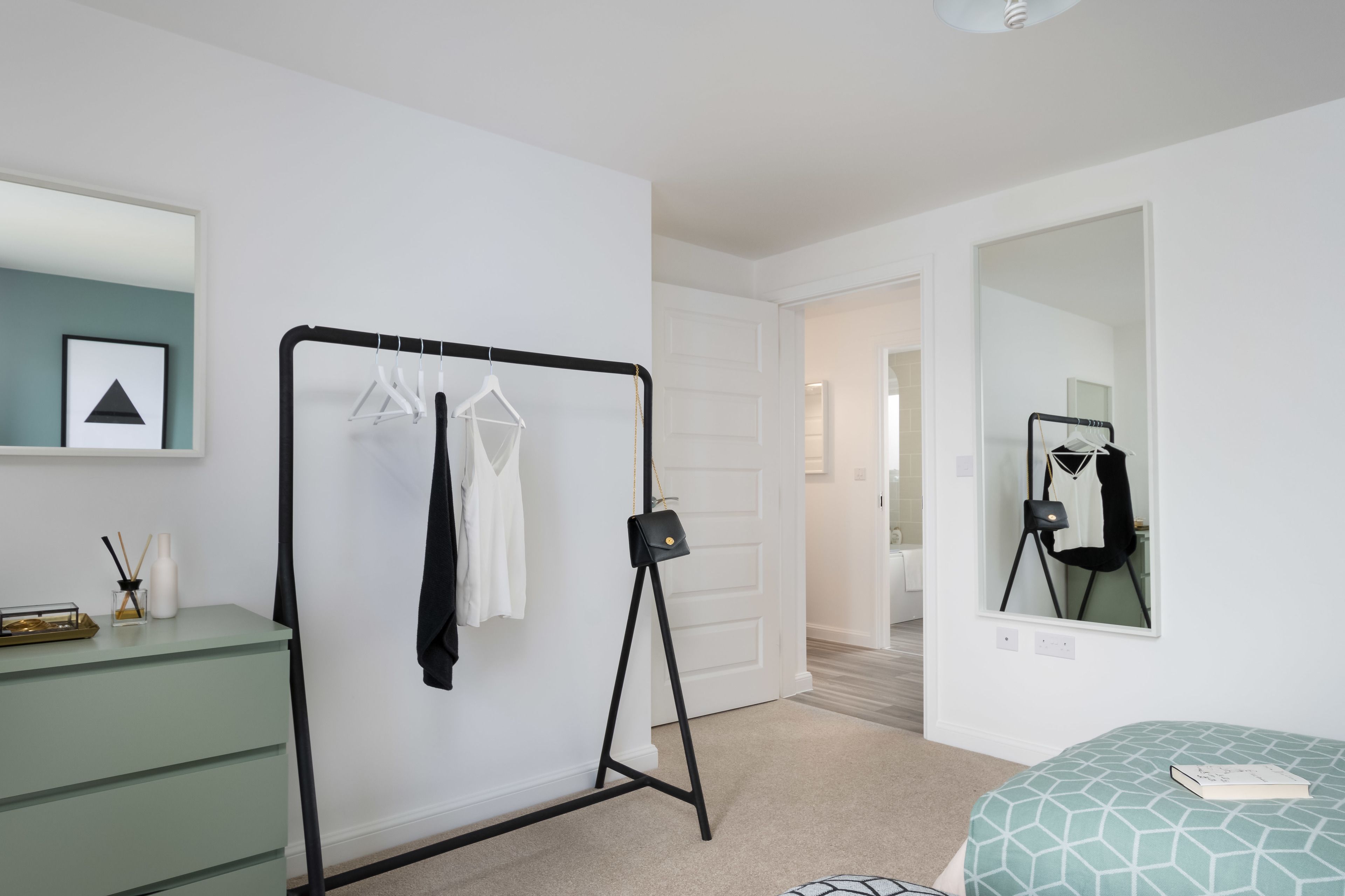 Une chambre à coucher avec un lit, une commode, un miroir et un portant à vêtements.