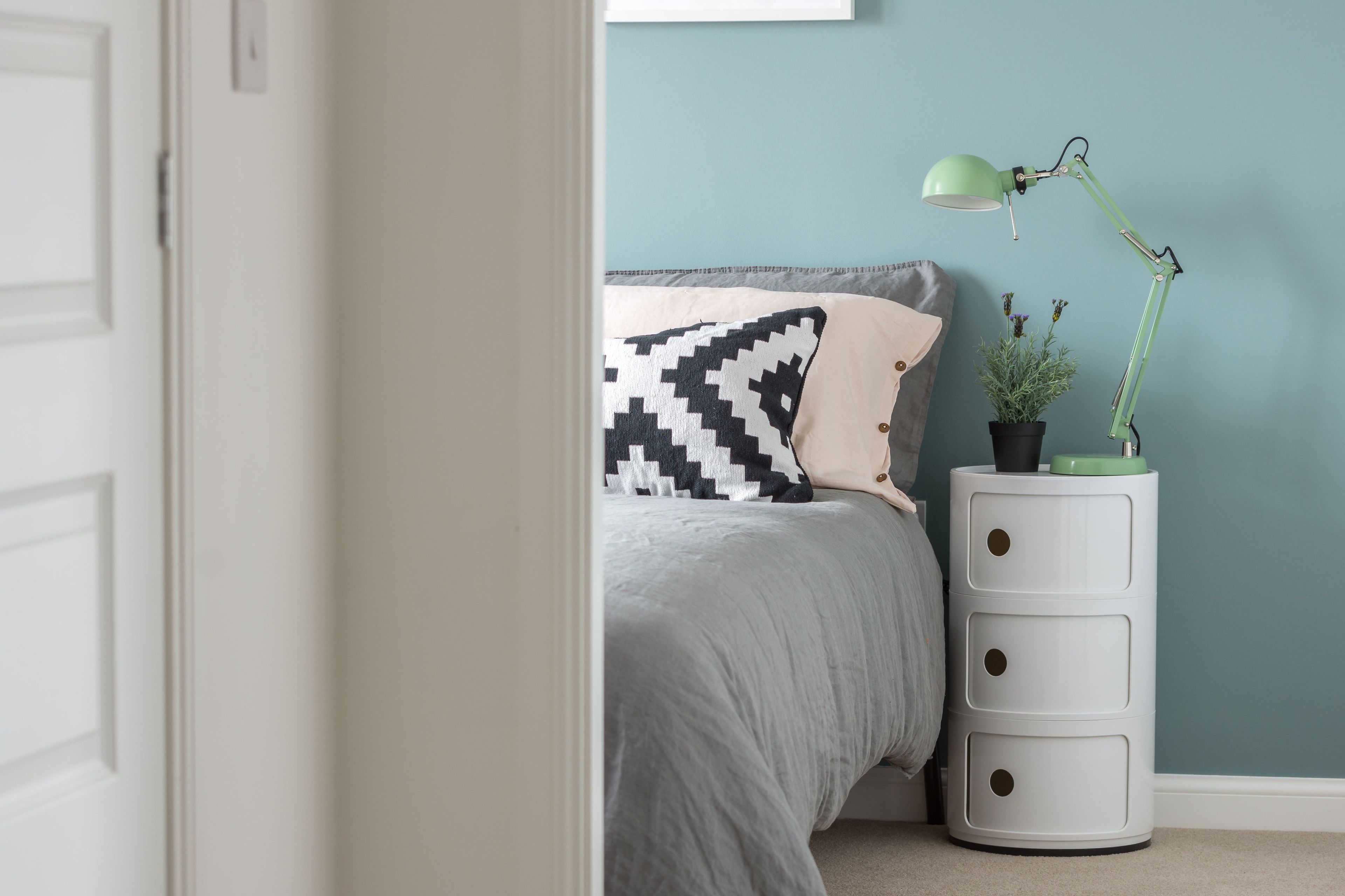 A bedroom with a bed, a nightstand with a lamp, and a potted plant.