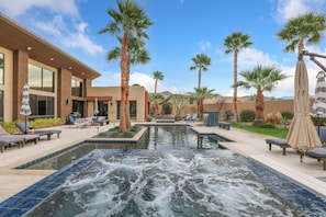 A pool area with a hot tub, lounge chairs, and palm trees.