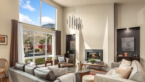 A modern living room with a fireplace, leather sofas, a coffee table, and a large window with a view of mountains. - Luxury Palm Springs Retreat. Pool, Spa & Stunning Mountain Views (Palm Springs)
