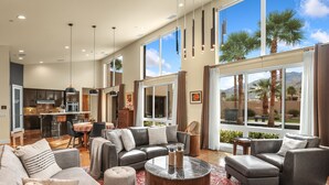 A spacious living area with a large window, a kitchen in the background, and a seating area with a coffee table. - Luxury Palm Springs Retreat. Pool, Spa & Stunning Mountain Views (Palm Springs)
