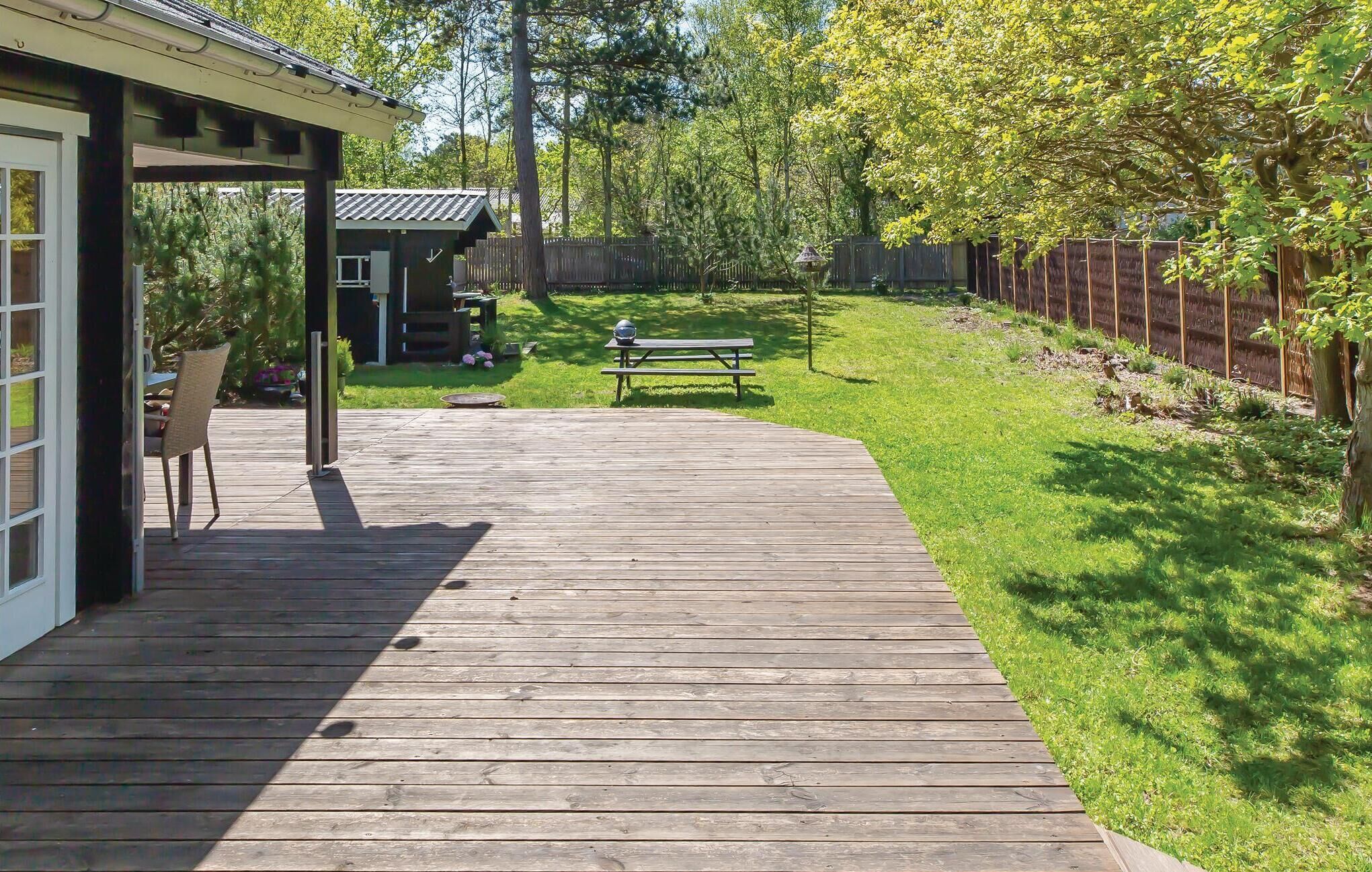 A wooden deck leading to a covered patio area with a table and chairs, surrounded by a grassy yard and a wooden fence.