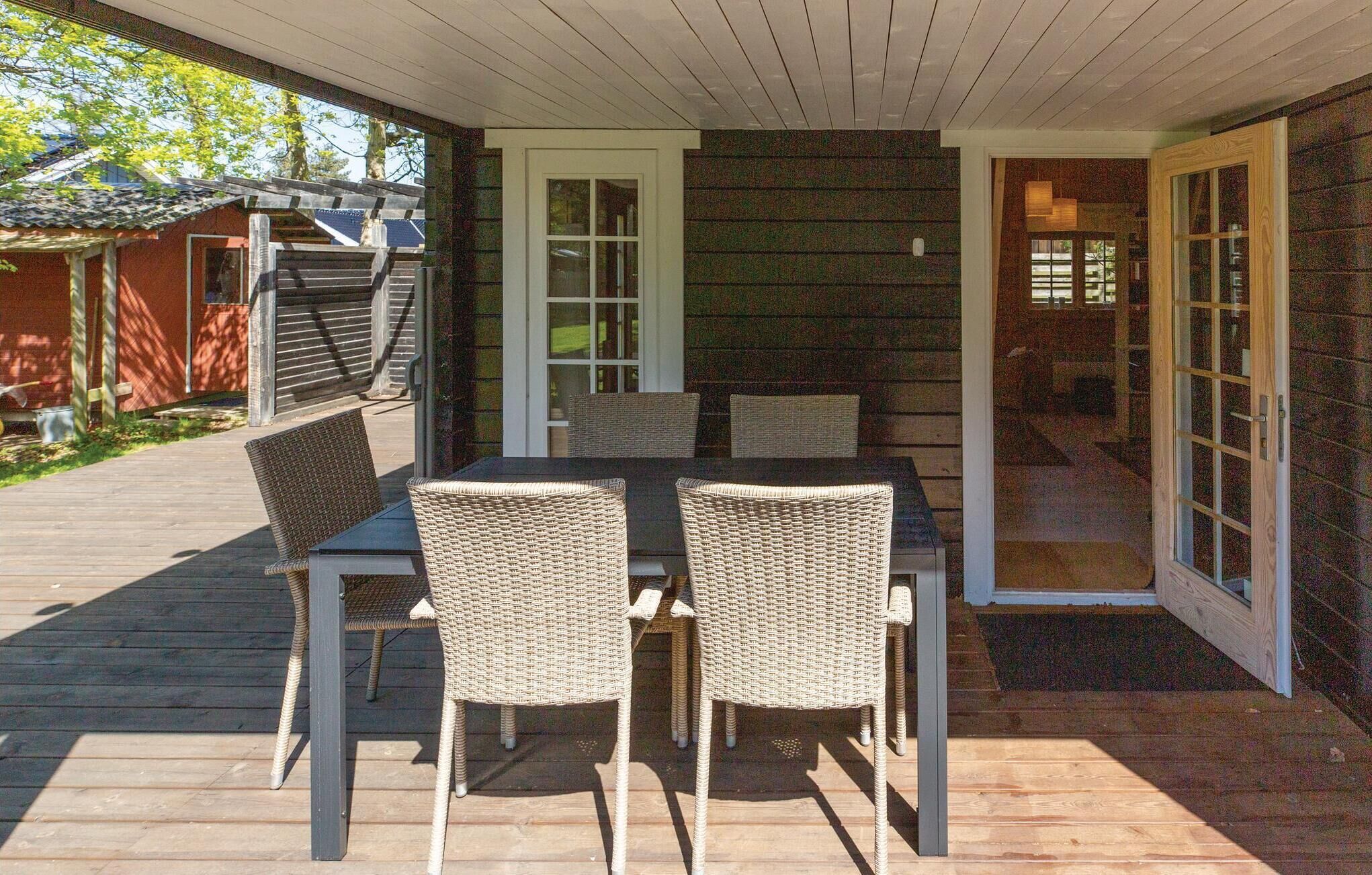 A covered outdoor dining area with a table and wicker chairs, a wooden deck, and a sliding glass door leading to a covered porch.