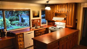 Cocina con armarios de madera, estufa, lavavajillas y un amplio ventanal con vistas a un jardín.
