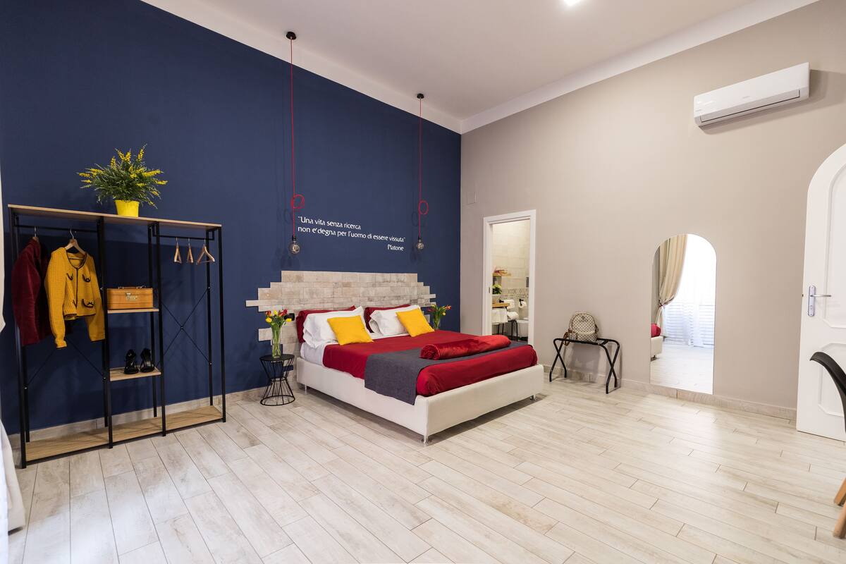 A modern bedroom with a bed, a wardrobe, a mirror, and a potted plant.