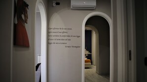 Un pasillo con una cita en la pared, una escalera y una cama al fondo.