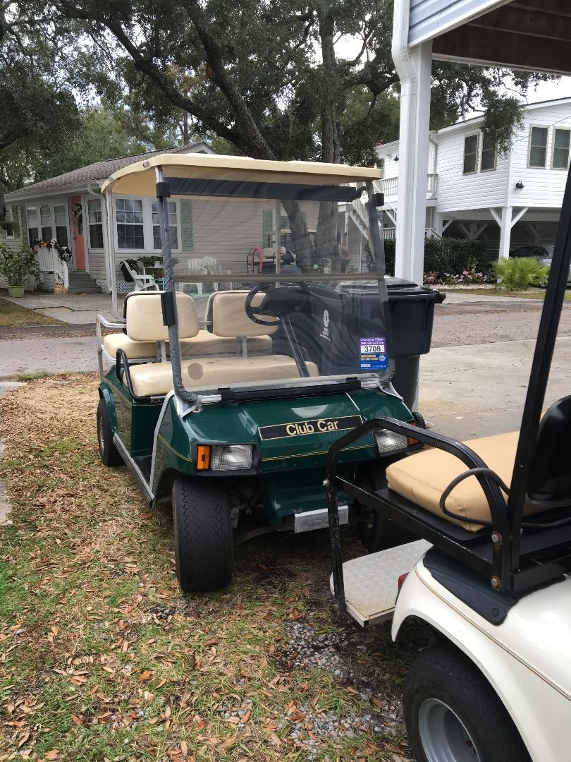 Un véhicule de golf vert, doté d’un auvent beige, est garé sur une pelouse.