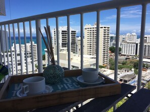 A balcony with a tray containing two white cups and a decorative vase, overlooking a cityscape with tall buildings and a clear blue sky. - Chic Bright Beautiful Studio with Ocean View CONDADO and parking (San Juan)