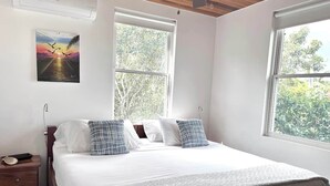 A bedroom with a large bed, two windows, a nightstand, and a painting on the wall. - Villa, Pool, AC, Dock and Beach access Paddle boards (Caye Caulker)