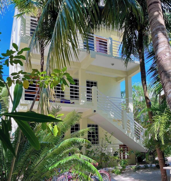 A multi-story building with balconies, surrounded by lush greenery and palm trees.