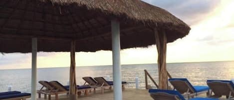 Un área de descanso frente a la playa, con terraza de madera y sombrillas de techo de paja, con vista al mar.