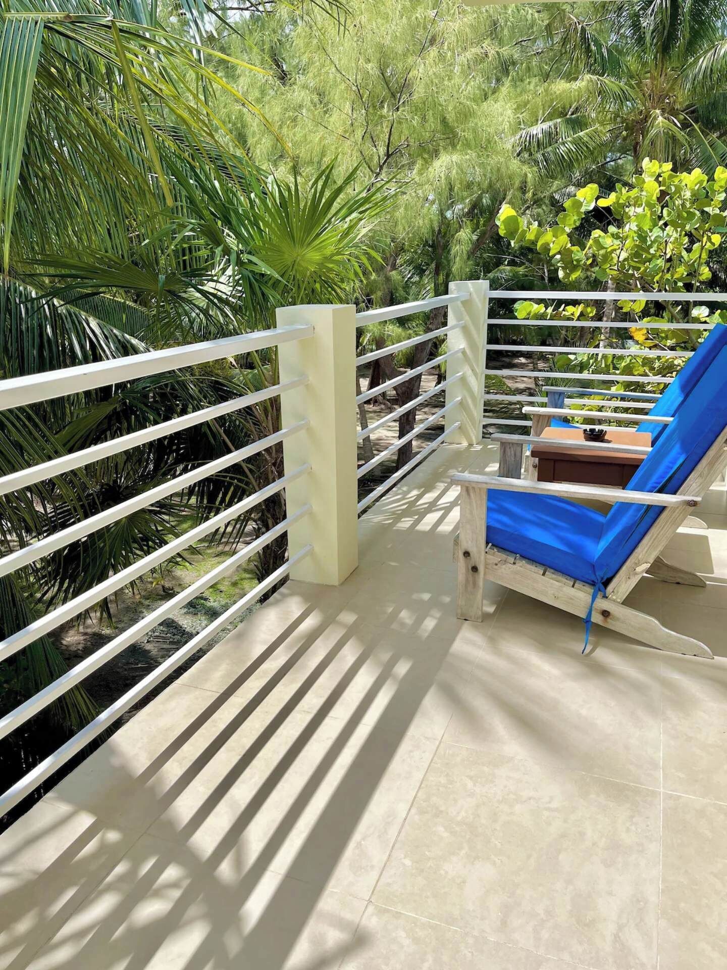 Een balkon met een blauwe loungestoel, een witte reling en weelderige begroeiing op de achtergrond.