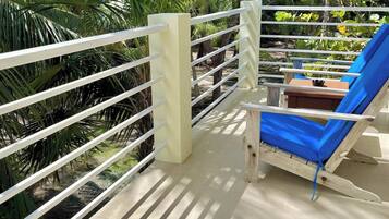 Een balkon met een blauwe loungestoel, een witte reling en weelderige begroeiing op de achtergrond.