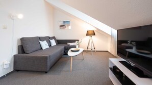 Una sala de estar moderna con un sofá gris, un televisor de pantalla plana, una lámpara y una mesita con un cuenco.