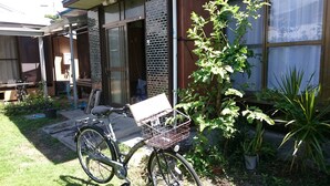 En cykel med en korg som står parkerad i ett bostadsområde med ett hus, ett garage och olika sorters krukväxter.