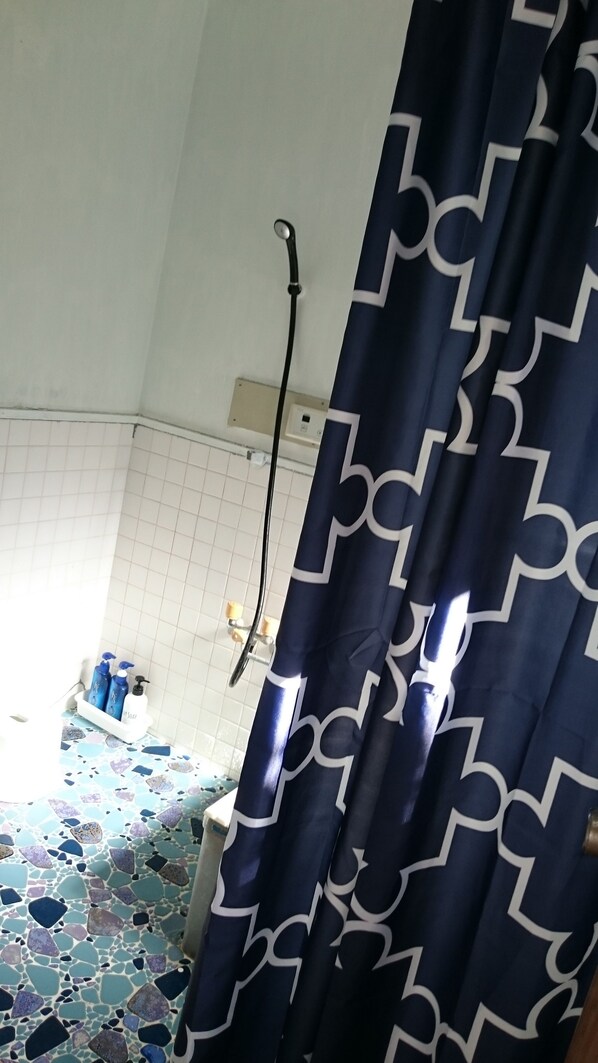 Un baño con cortina de ducha, pared de azulejos y ducha.
