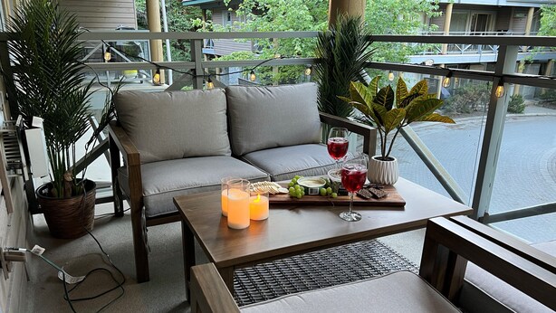 A balcony with a sofa, a table with drinks and snacks, and potted plants.