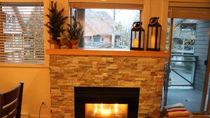 A fireplace with a stone facade, a window with blinds, and a view of the outside.