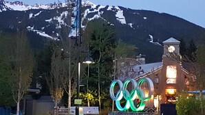 A building with Olympic rings illuminated in front of a mountain backdrop.