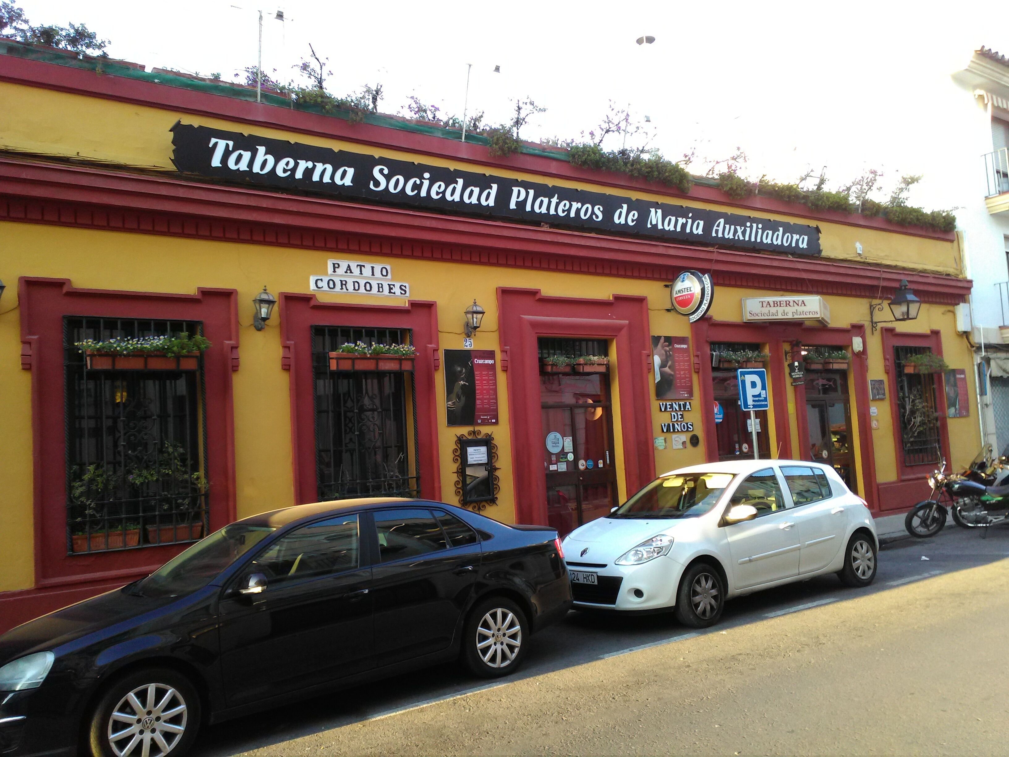 Un bâtiment à la façade jaune et aux ornements rouges, sur lequel on peut voir les enseignes « Taberna Sociedad Plateros de Maria Auxiliadora » et « Patio Cordobes ».