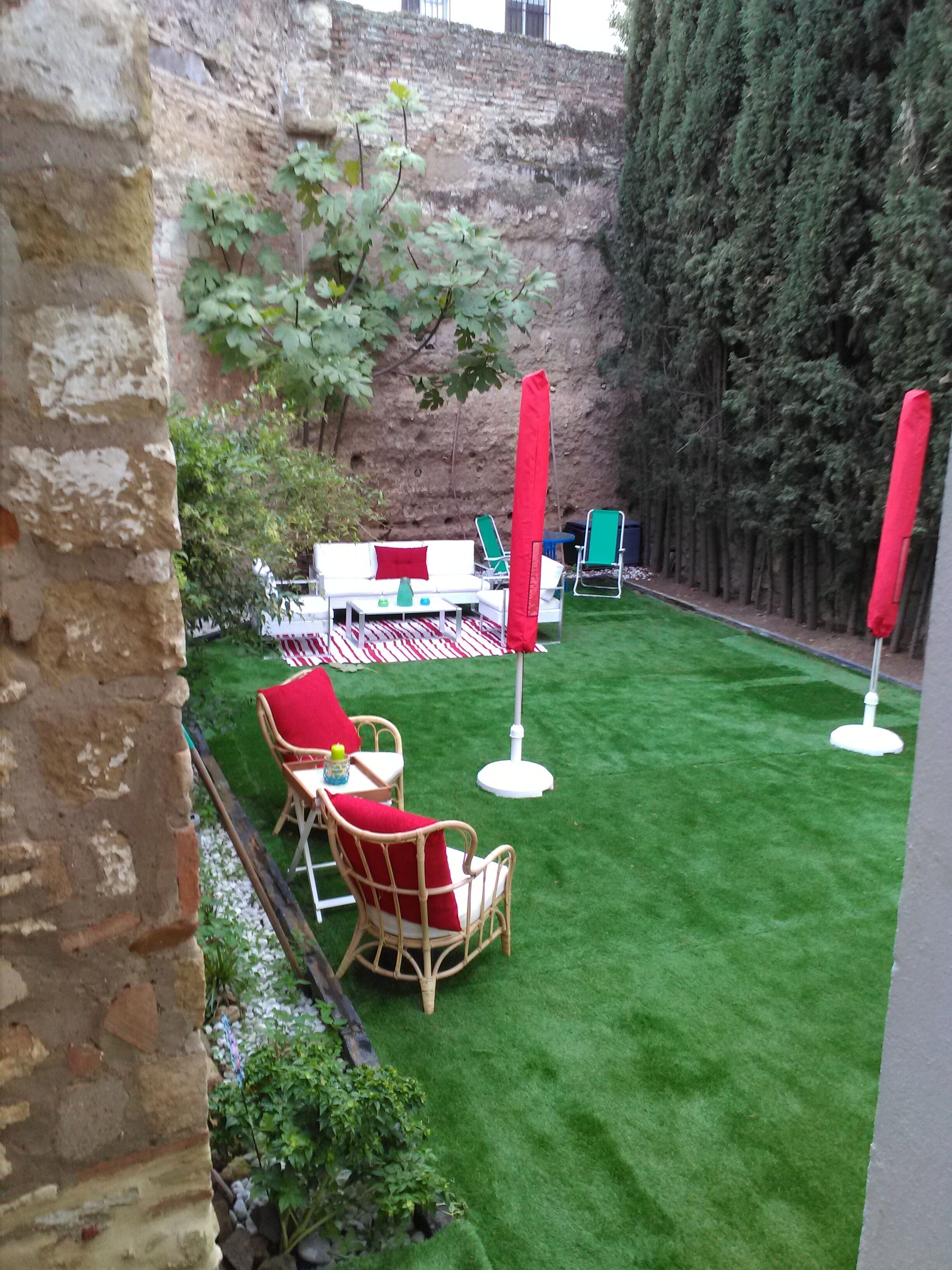 Un'area patio con un tavolo e sedie bianche, ombrelloni rossi e un prato verde.