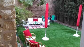 Un'area patio con un tavolo e sedie bianche, ombrelloni rossi e un prato verde.