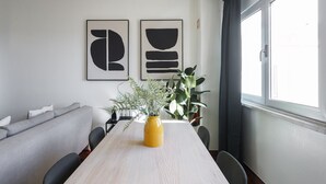 Ein moderner Essbereich mit einem Holztisch, Stühlen, einer gelben Vase mit Pflanzen und abstrakter Wandkunst.