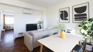 Ein modernes Wohnzimmer mit einer Couch, einem Esstisch und einem Fernseher. Auf dem Tisch steht ein Blumentopf.