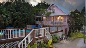 A pink house with a balcony, surrounded by lush greenery and a clear sky. - Oceanview/Pool/Dock/AC-Barbaras Beach House-3 bed/2 bath sleeps 7 (Caye Caulker)
