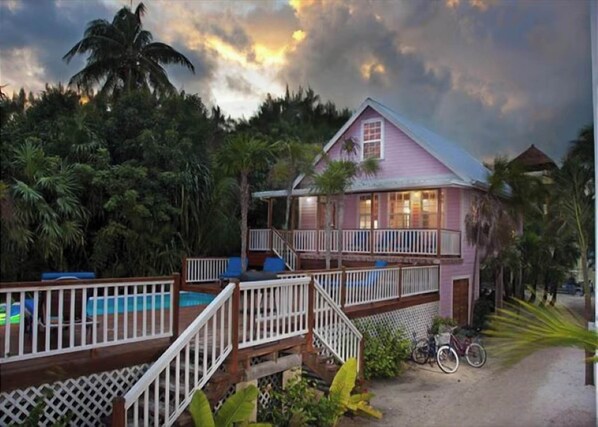 A pink house with a balcony, surrounded by lush greenery and a clear sky.