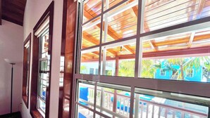 A corridor with large windows, wooden ceiling beams, and a view of outdoor seating and a blue building. - Oceanview/Pool/Dock/AC-Barbaras Beach House-3 bed/2 bath sleeps 7 (Caye Caulker)