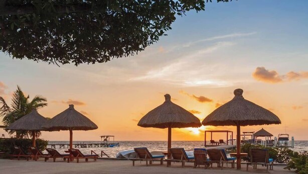 A beach with thatched umbrellas and lounge chairs, a pier, and boats in the background during sunset. - Oceanview/Pool/Dock/AC-Barbaras Beach House-3 bed/2 bath sleeps 7 (Caye Caulker)