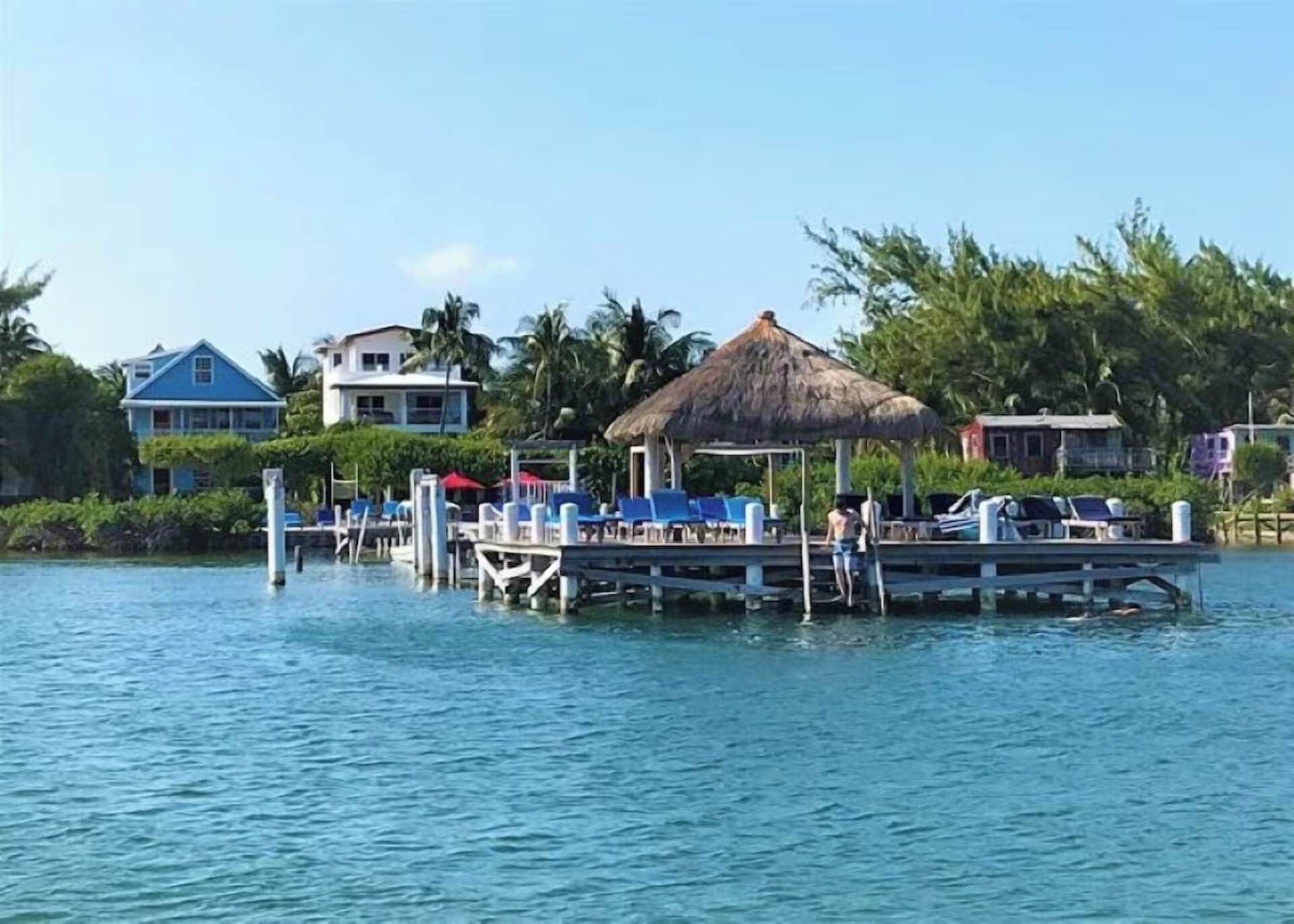A waterfront resort with a dock, lounge chairs, and a thatched-roof structure.