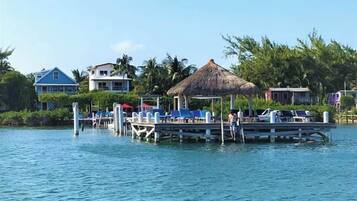 A waterfront resort with a dock, lounge chairs, and a thatched-roof structure.