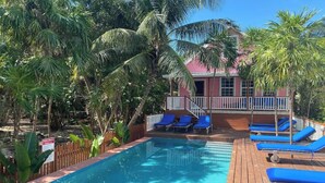 A pool area with blue lounge chairs, a wooden deck, and a pink building with a white railing. - Oceanview/Pool/Dock/AC-Barbaras Beach House-3 bed/2 bath sleeps 7 (Caye Caulker)