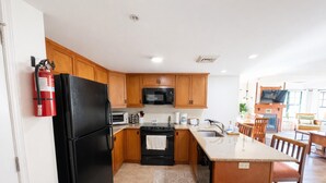A modern kitchen with wooden cabinets, a black refrigerator, a microwave, and a stove. There is a fire extinguisher mounted on the wall.