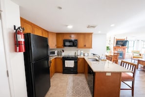 A modern kitchen with wooden cabinets, a black refrigerator, a microwave, and a stove. There is a fire extinguisher mounted on the wall. - Heated Pool Hot Tubs Sauna Gym Deck Mtn Front Appalachian @ Mtn Creek #248 (Vernon)