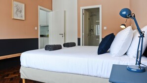 A hotel room with a bed, a desk with a lamp, a door, and a framed picture on the wall. - Negroni Balcony in Lisbon - by Misha's Place (1A) (Lisboa ciudad)