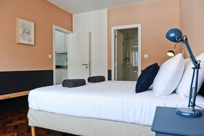 Une chambre d’hôtel avec un lit, un bureau doté d’une lampe, une porte et un tableau encadré au mur.