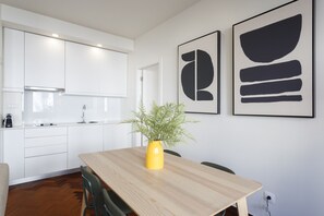 Una cocina moderna con armarios blancos, una mesa de comedor de madera y un jarrón amarillo con una planta.