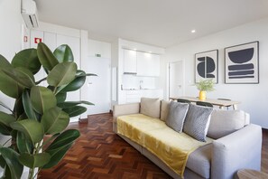 Quarto de hotel moderno com sofá, mesa de jantar e área de cozinha ao fundo.