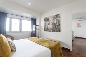 Una habitación de hotel con cama, un banco, una obra de arte floral grande en la pared y una ventana con cortinas.