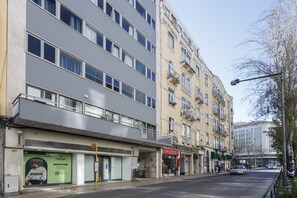 Un immeuble à plusieurs étages doté d’une façade moderne, d’un commerce au rez-de-chaussée et d’une rue animée par la circulation des voitures et des piétons.